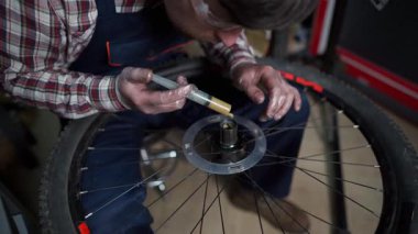 Bir atölyede profesyonel bir tamirci dağ bisikletini tamir ediyor, merkeze ve yönlere odaklanıyor. İş kıyafetleri giyer, düzgün performans sağlamak için uzman hizmeti, yağlama ve bakım sağlar.. 