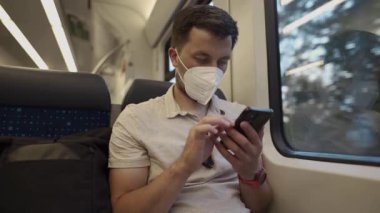 Alman treninin içinde akıllı telefon kullanan maskeli bir adam. Salgın yaşamın modern bir yansıması, dijital bağlılık, şehir içi iş seyahati ve hastalıklara karşı kişisel koruma