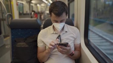 Beyaz tişörtlü ve kırmızı saatli bir adam korunmak için telefonunu toplu taşıma aracında karıştırıyor. Kentsel Avrupa ortamlarında bir sağlık krizi sırasında güvenli seyahat yakaladı. 