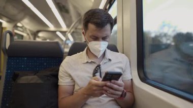 Tıbbi maskeli genç bir erkek yolcu Münih 'te akşam treninde akıllı telefonuna bakıyor. Fotoğraf sağlık bilinci, modern seyahat ve günlük rutini yansıtıyor.. 