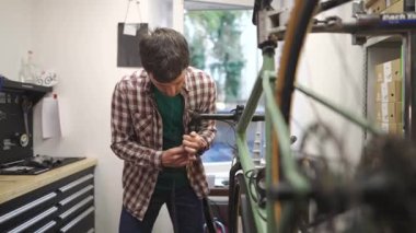 Bisiklet tamircisi bisiklet tamir atölyesindeki çalışma yerinde bisiklet gidonu etrafına bisiklet bandı sarar. Bisiklet mühendisi gidon bandı atölyedeki iş yerinde çakıl bisikleti üzerinde. 