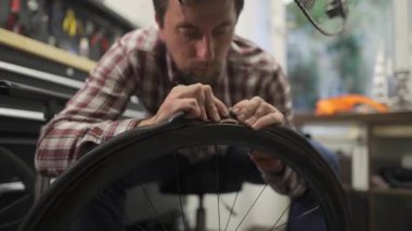 Erkek bisiklet tamircisi, iyi donanımlı bir tamirhanede yüksek performanslı bir otoyol bisikletinin lastiğini dikkatlice değiştiriyor. Etrafında bir sürü araç gereç, yedek parça ve düzenli ekipmanlar var.. 