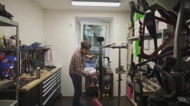 Erkek bisiklet tamircisi bir bisiklet atölyesinde servisten sonra bisikleti temizleyip tamir ediyor. Konferansta en iyi performans ve durumu sağlamak için motor onarımı, bakım ve onarım sonrası temizlik üzerinde duruluyor. 
