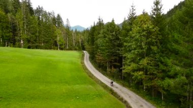 Eylül ayında Almanya 'nın Bavyera şehrinde çakıl bisikleti süren erkek bisikletçinin hava manzarası. Arkasından bisikletlinin drone görüntüsü dağlardaki Bavyera ormanında çakıllı bisiklet rotası boyunca gidiyor.. 