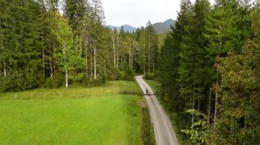 Eylül ayında Almanya 'nın Bavyera şehrinde çakıl bisikleti süren erkek bisikletçinin hava manzarası. Arkasından bisikletlinin drone görüntüsü dağlardaki Bavyera ormanında çakıllı bisiklet rotası boyunca gidiyor.. 