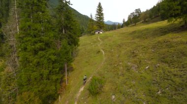 Sonbahar boyunca dağlarda yokuş yukarı uçan çakıl bisikletli bisikletçilerin hava manzarası. Yeşil çayırları, ormanı ve ücra kulübesi olan manzaralı bir yer. Macera, özgürlük, doğa, spor ve dayanıklılık. 