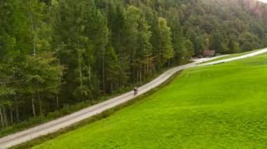 Eylül ayında Almanya 'nın Bavyera şehrinde çakıl bisikleti süren erkek bisikletçinin hava manzarası. Arkasından bisikletlinin drone görüntüsü dağlardaki Bavyera ormanında çakıllı bisiklet rotası boyunca gidiyor.. 
