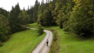 Eylül ayında Almanya 'nın Bavyera şehrinde çakıl bisikleti süren erkek bisikletçinin hava manzarası. Arkasından bisikletlinin drone görüntüsü dağlardaki Bavyera ormanında çakıllı bisiklet rotası boyunca gidiyor.. 