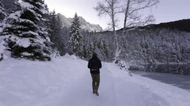 Eibsee-Rundweg. Mann wandert im Wintermorgen auf dem verschneiten Eibsee Rundweg, Bayern, Deutschland 'de. Blick auf die Zugspitze, verschneite Baeume, Ruhe und Natur pur im Wettersteingebirge erleben. 