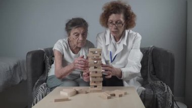 Jenga oynayan yaşlı kadın, bloklardan kule inşa ediyor. Beyaz laboratuvar önlüklü yaşlı doktor, kıdemli hastayı destekliyor, mantık geliştiriyor, iyi motor beceriler geliştiriyor, evde yaşlı yalnız kadın hastalıkları var..