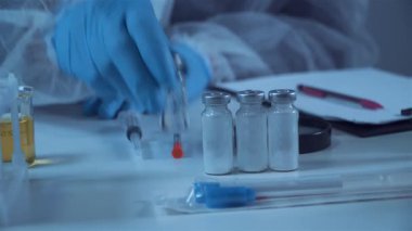 Steril bir laboratuvarda şırınga kullanarak şişeden sıvı alan bir bilim adamının yakın çekimi. Aşı geliştirme, ilaç araştırmaları, tıbbi testler ve biyoteknoloji kavramı.