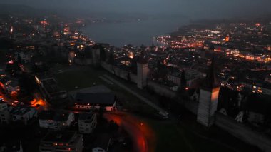 Musegg Wall ve dokuz kulesi geceleri İsviçre 'nin Lucerne kentindeki parlayan şehre bakıyor. Lucerne 'in ortaçağ savunması. Museggmauer Luzern und ihre neun Tuerme Luftaufnahme bei Nacht. 