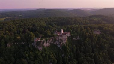Lichtenstein Şatosu 'nun üzerinde, Baden-Wuerttemberg, Deutschland' deki Albtrauf uçurumlarına tünemiş sihirli insansız hava aracı günbatımı. Yazın bu 19. yüzyıl dağ kalesinin havadan görünüşü. Marchenschloss Wurttembergs