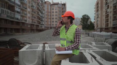 İnşaat mühendisi yüksek binalardaki beton binalarda, başlık takarak oturuyor. Yemek molasında, dışarıda dinleniyor, temiz havanın tadını çıkarıyor, kahve içiyor, telefonda konuşuyor.. 