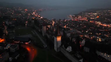 Musegg Wall ve dokuz kulesi geceleri İsviçre 'nin Lucerne kentindeki parlayan şehre bakıyor. Lucerne 'in ortaçağ savunması. Museggmauer Luzern und ihre neun Tuerme Luftaufnahme bei Nacht. 