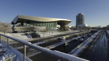 Karlı Münih, Almanya. BMW Welt, BMW Kulesi ve karargah parlak kış güneşi altında parlıyor. Modern mimari şehir zarafetiyle buluşuyor, karla kaplı sokaklar ve berrak mavi gökyüzü. Kış şehri