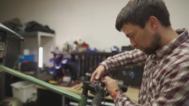 Bisikletli tamirci atölyesindeki çakıl bisikletinin gidon bandına sarılmış. Bisiklet teknisyeni kaseti dikkatlice gidonun etrafına sarar ve atölyede bakım yapar.. 