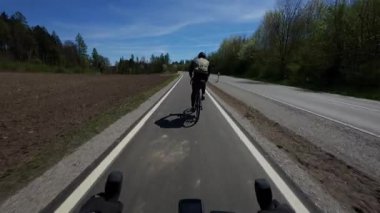 Almanya 'nın kırsalında yeni inşa edilmiş bir bisiklet yolunda bisiklet süren bir bisikletçi. Taze, asfaltlı bisiklet yolu kasabalar arasında güvenli, çevre dostu bir ulaşım sağlar ve doğal orman manzarasıyla harmanlanır.