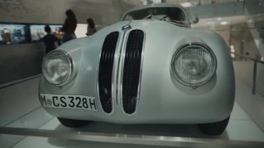 20 Nisan 2022. Münih, Almanya. Münih 'teki BMW Müzesi' ndeki turistler, modern bir sergi salonundaki zarif ve ender bulunan BMW 328 spor arabayı yakından inceleyerek otomotiv tarihini deneyimliyorlar.. 