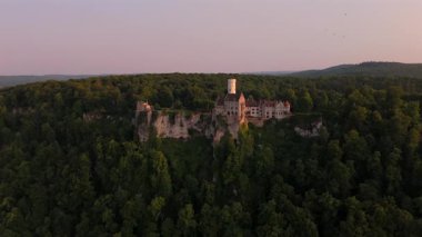 Luftaufnahme Schloss Lichtenstein am Albtrauf bei Sonnenuntergang. Maerchenhafte Architektur auf einem Felsen uber dem Neckar-Nebenfluss im Landkreis Reutlingen, Baden-Wuerttemberg, Deutschland. 