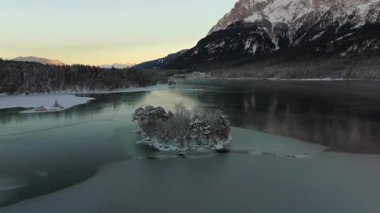 Ludwigsinsel, Heissenbuechel 'in Garmisch-Partenkirchen, Bayern, Deutschland yakınlarındaki donmuş Eibsee üzerindeki hava manzarası. Sakin kış sabahı karla kaplı ağaçları ve buz gibi gölü vurguluyor.. 
