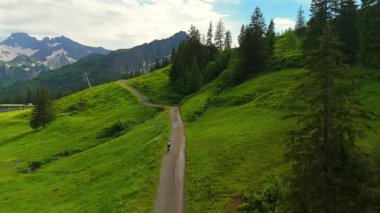 Yazın Alpler 'de kayak merkezinde bisiklet süren hava manzaralı bisikletçi. Bisikletçi Almanya 'nın Bavyera dağlarındaki dağ tatil beldesinde çakıllı bisikletle seyahat ediyor. Alp yamaçlarında bisiklet gezileri