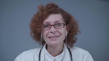 Kulaklık takmış yaşlı kadın pratisyen kamerayla görüntülü görüşme yapıyor, hastaya görüntülü konuşma yoluyla danışmanlık yapıyor. Doktor görüntülü görüşme için danışmanlık yapıyor. Web kamerasından görüntüle.