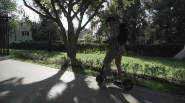 Parkta elektrikli scooter kullanan bir adam. Genç bir erkek, güneşli bir günde elektrikli scooter kullanıyor. Ekolojik ulaşım konsepti. Yaşam tarzı. Modern vatandaş eko elektrikli scooterla seyahat ediyor..