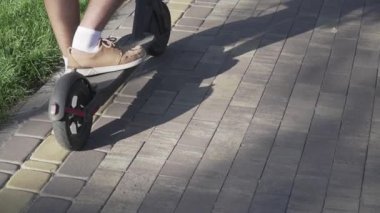 Parkta elektrikli scooter kullanan bir adam. Genç bir erkek, güneşli bir günde elektrikli scooter kullanıyor. Ekolojik ulaşım konsepti. Yaşam tarzı. Modern vatandaş eko elektrikli scooterla seyahat ediyor..