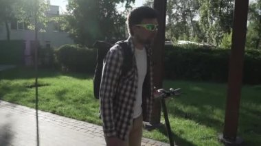 Parkta elektrikli scooter kullanan bir adam. Genç bir erkek, güneşli bir günde elektrikli scooter kullanıyor. Ekolojik ulaşım konsepti. Yaşam tarzı. Modern vatandaş eko elektrikli scooterla seyahat ediyor..