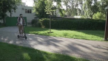 Modern vatandaş kaldırımda eko elektrikli scooterla seyahat ediyor. Ekolojik ulaşım. Elektrikli scooter kullanan genç bir adam. Scooter kiralama servisi. Beyaz erkek, parkta elektrikli taşıma aracında..