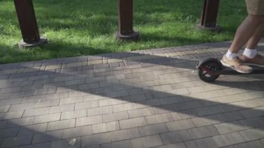 Ekose gömlekli, güneş gözlüklü, güneşli bir parkta, yaz havasında elektrikli scooter süren beyaz bir adam. Konu ekolojisi, çevre koruma, araba egzoz gazlarından kaynaklanan hava kirliliği. Eko taşımacılığı.