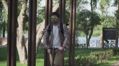 Parkta elektrikli scooter kullanan bir adam. Genç bir erkek, güneşli bir günde elektrikli scooter kullanıyor. Ekolojik ulaşım konsepti. Yaşam tarzı. Modern vatandaş eko elektrikli scooterla seyahat ediyor..