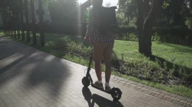 Modern vatandaş kaldırımda eko elektrikli scooterla seyahat ediyor. Ekolojik ulaşım. Elektrikli scooter kullanan genç bir adam. Scooter kiralama servisi. Beyaz erkek, parkta elektrikli taşıma aracında..