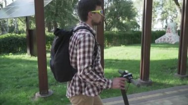 Modern vatandaş kaldırımda eko elektrikli scooterla seyahat ediyor. Ekolojik ulaşım. Elektrikli scooter kullanan genç bir adam. Scooter kiralama servisi. Beyaz erkek, parkta elektrikli taşıma aracında..