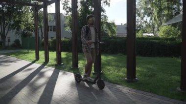 Modern vatandaş kaldırımda eko elektrikli scooterla seyahat ediyor. Ekolojik ulaşım. Elektrikli scooter kullanan genç bir adam. Scooter kiralama servisi. Beyaz erkek, parkta elektrikli taşıma aracında..