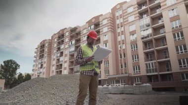 İnşaat alanının planlarını okuyan bir müteahhit. İnşaat halinde. Korumalı iş kıyafetleri alanında çalışan profesyonel mühendis konut inşaatı planını inceliyor..