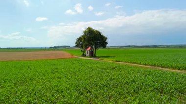 Küçük şapel toprak yolların kesiştiği yerde gölgeli ağacın altındaki ekin tarlalarıyla çevrili. Yazın insansız hava aracı manzarası huzurlu kırsal manzarayı yakalar, sükunetini ön plana çıkarır..