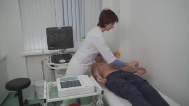 Elektrokardiyogram için tıbbi ekipman. Erkek hastaya EKG testi yapan doktorlar. Kalp krizi teşhisi, taşikardi. Elektrokardiyografi prosedürü. Kardiyolog kontrol testi yapıyor..