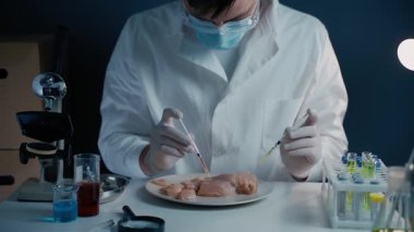 Erkek beslenme uzmanı gıda ürünlerini laboratuvarda test ediyor. Laboratuvar asistanı GDO tavuğunu test ediyor. Tavuk etini test etmek için kimyasalı enjekte ediyorum. Genetik olarak değiştirilmiş gıda, şırınga.