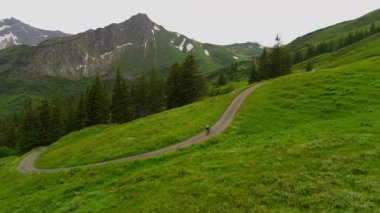 Yazın Alpler 'de kayak merkezinde bisiklet süren hava manzaralı bisikletçi. Bisikletçi Almanya 'nın Bavyera dağlarındaki dağ tatil beldesinde çakıllı bisikletle seyahat ediyor. Alp yamaçlarında bisiklet gezileri