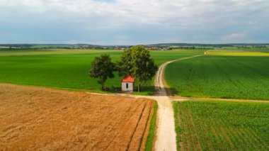 Küçük şapel toprak yolların kesiştiği yerde gölgeli ağacın altındaki ekin tarlalarıyla çevrili. Yazın insansız hava aracı manzarası huzurlu kırsal manzarayı yakalar, sükunetini ön plana çıkarır..