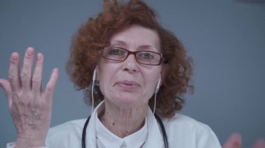 Steteskoplu, kulaklık takmış, sanal sohbetteki hastaya bakan profesyonel bir kadın doktor. Hekimler video uygulaması danışmanlığı kullanırlar. Web kamerası görünümü.