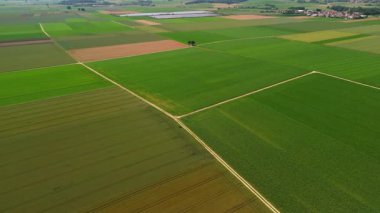 Almanya 'da yaz boyunca Bavyera tarım arazilerinin havadan görünüşü. Yeşil alanlar, toprak yollar ve kavşaktaki küçük şapel. Arka plandaki güneş panelleri sürdürülebilir tarım ve yenilenebilir enerjiyi vurguluyor. 