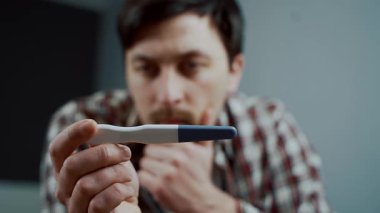 Bir adam, karısının ona yaptığı hamilelik testine bakar ve başını dertten tutar. Yüzündeki ifade endişe ve hayal kırıklığını gösteriyor. Beklenmedik hamileliğin onu rahatsız ettiğini açıkça gösteriyor.