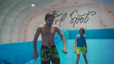 Flow Rider 'da çocuk ve eğitmen. Kapalı alanda sörf eğitimi almış. Su sörfü eğitimi alan bir genç. İçeride dalga simülatörü eğitimi alıyor. Genç sörfçü, üretilmiş dalgalar üzerine eğitim alırken. Su sporları.