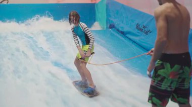 Çocuklar için kapalı sörf kulübü. Tema aktif eğlence ve su üzerinde ekstrem spor. Öğrenci ve koç dalga simülatöründe sörf eğitimi alıyor. Su parkında sörf tahtası..