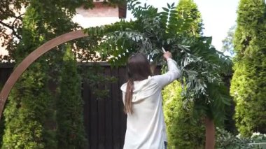 Profesyonel çiçekçi düğün kaydı için festival kemerini dekore ediyor. Kadın düğün dekoru kuruyor. Dekoratör, açık hava düğün törenini çiçekler ve yeşilliklerle süslüyor..