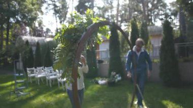 Çiçekçiler biner, düğün töreni için çiçek kemeriyle süslerler. Dekoratörler etkinlikte çalışıyor, doğum günü, yıldönümü, parti. Taze çiçeklerle süslenmiş bir olay. Kırsal tarzda. İşteki tasarımcı.