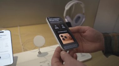 2 Ekim 2025. Münih, Almanya. Bir adam Almanya 'daki bir Apple mağazasında yeni gümüş iPhone 17 Pro' yu keşfediyor. Yakınlarda, AirPods Max kulaklıkları Apple cihazlarının modern teknoloji gösterimini tamamladı
